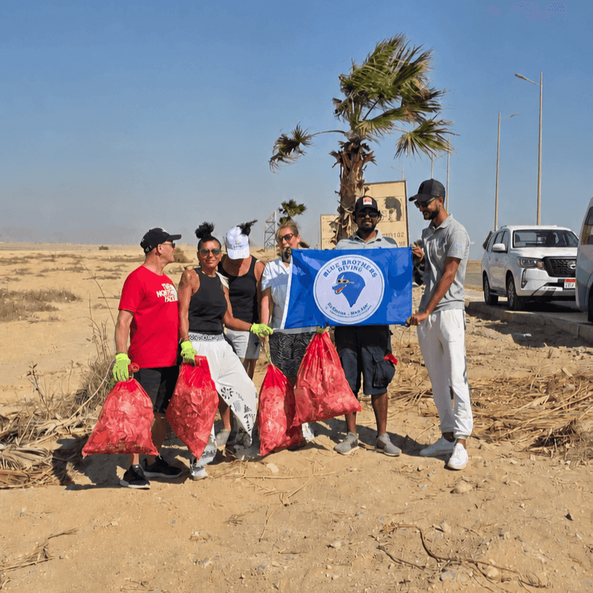 A group of volunteers holding red trash bags and a blue flag after a cleanup event.