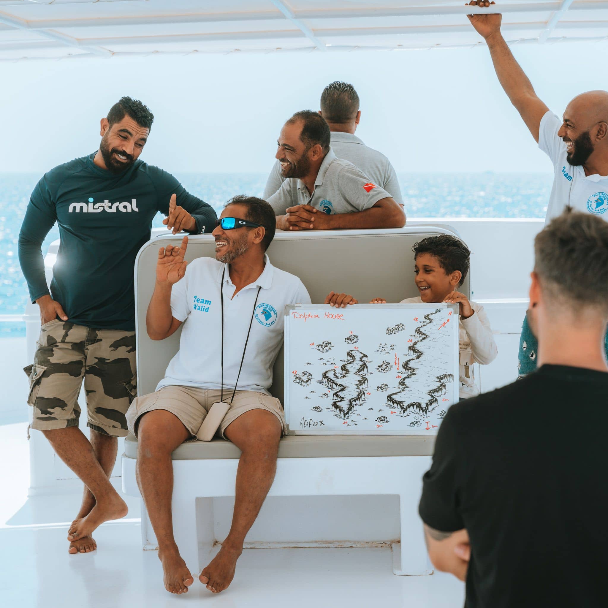 Diverse group of men and a boy on a boat looking at a drawing.