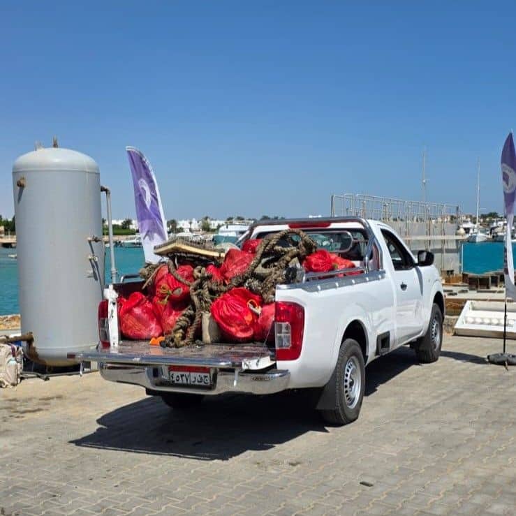 White pickup truck filled with red bags and marine debris at a sunny marina.