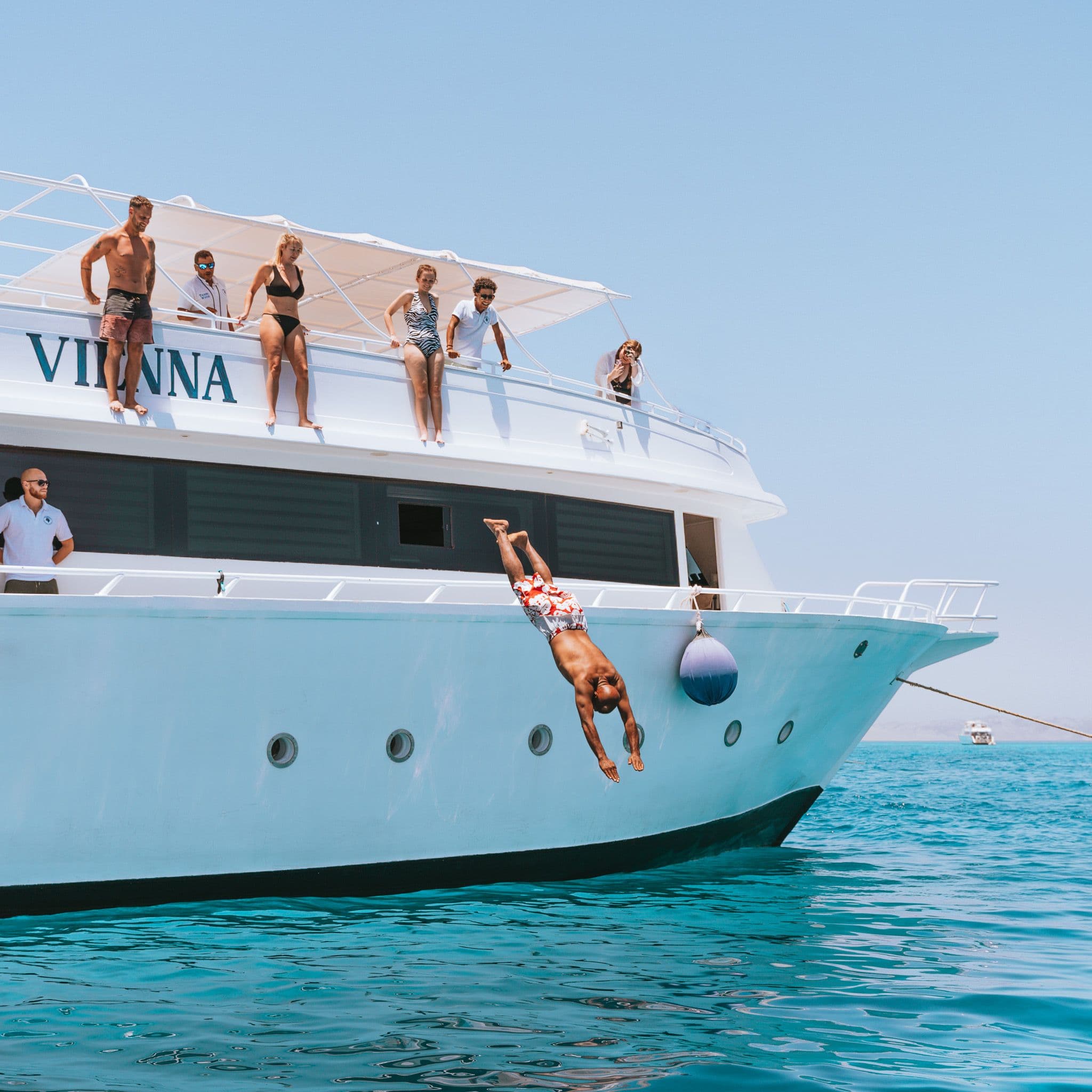 Person diving headfirst from a white yacht named VIANNA into clear turquoise water.