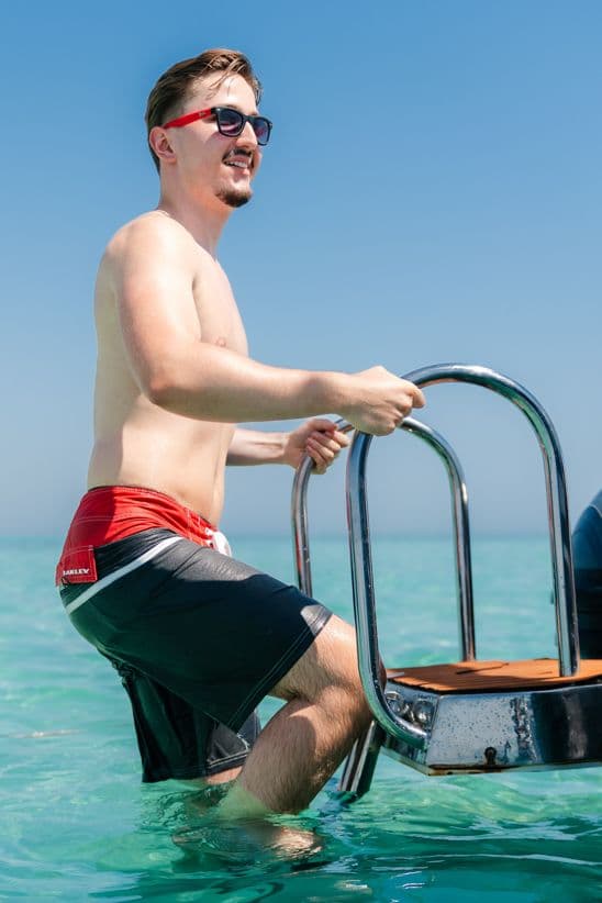 Mann steigt aus türkisblauem Wasser über die Bootsleiter an Bord