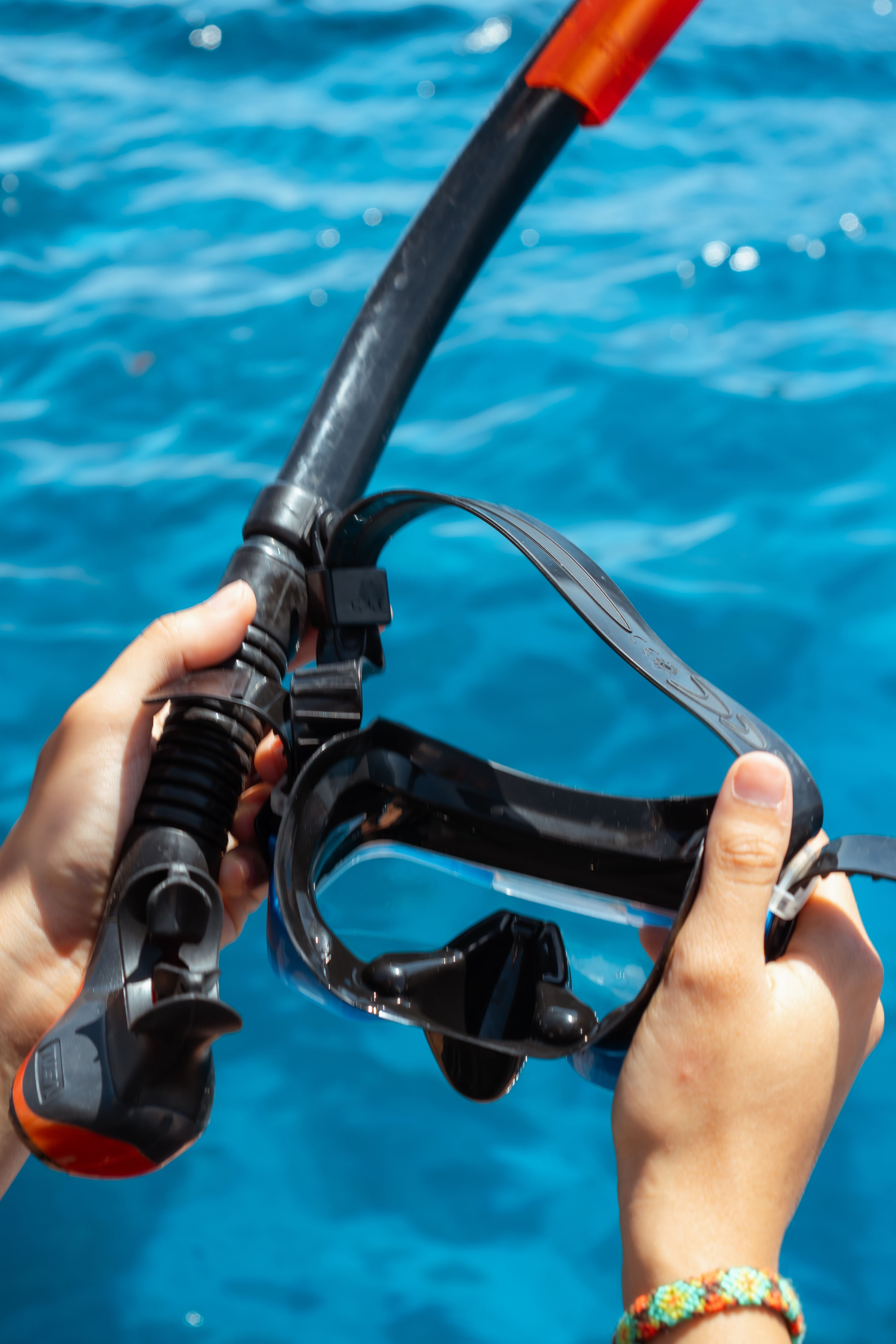Hands holding a black snorkel and mask against a backdrop of clear blue water.